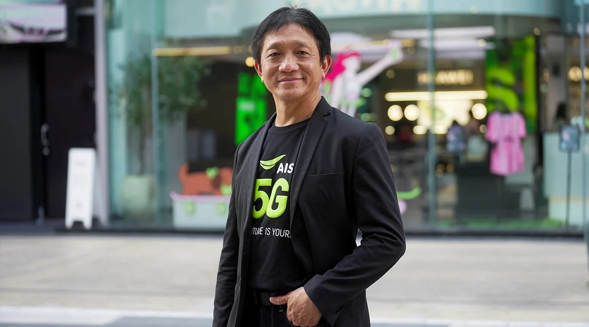 ผู้บริหารชายสวมเสื้อสีดำสกรีน AIS 5G ยืนอยู่หน้าอาคารกระจกกลางเมือง