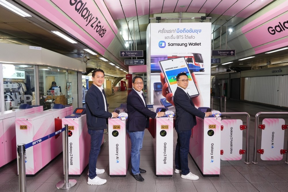ชายสามคนยืนที่ประตูเก็บค่าโดยสาร BTS ข้างป้าย Samsung Wallet แตะขึ้น BTS ได้แล้ว